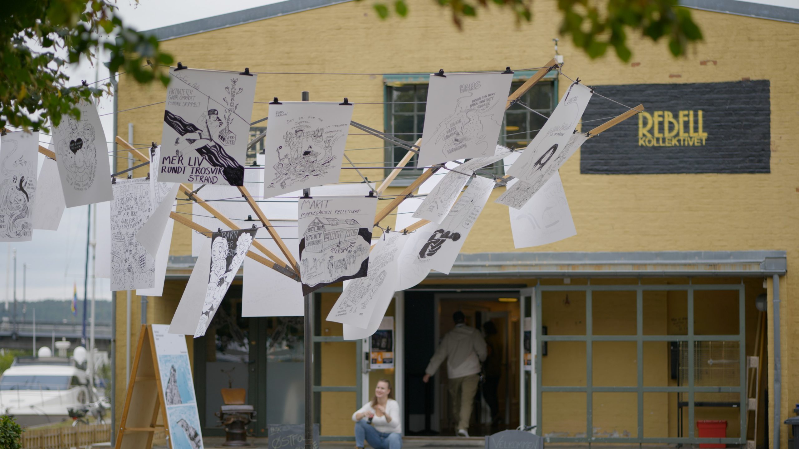 In Search of Democracy 3.0 Fredrikstad: Bilde av mange tegninger hengende hengende i installasjons som ligner et tørkestativ
